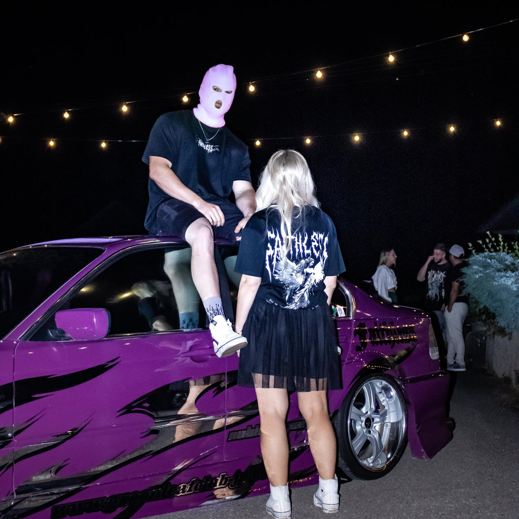 Black Angel tee worn at a night meet, back print with angel and Faithless lettering, next to a purple BMW