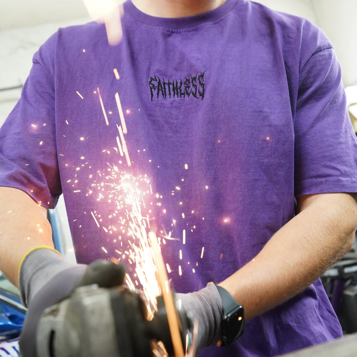 Shadow tee in washed purple worn while cutting steel, sparks in front of the Faithless chest embroidery